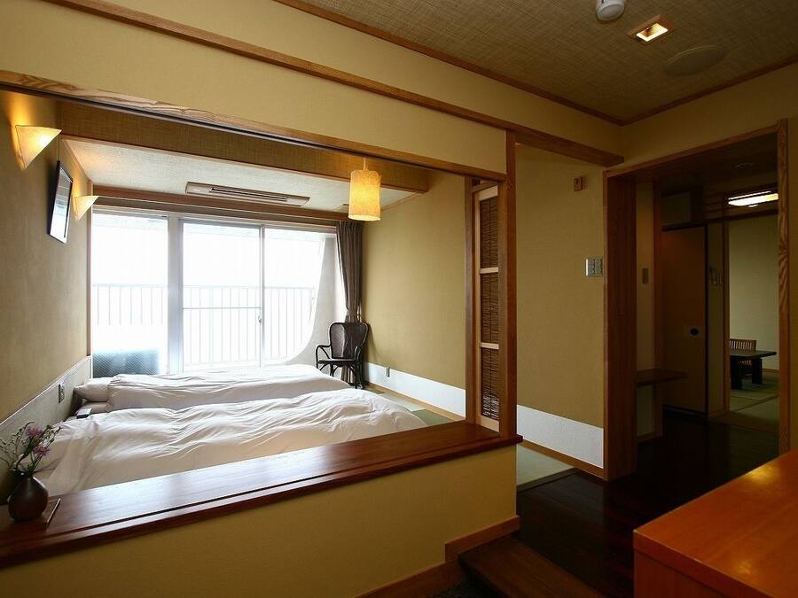 A hotel room with a bed, bedside table, and a window with curtains.