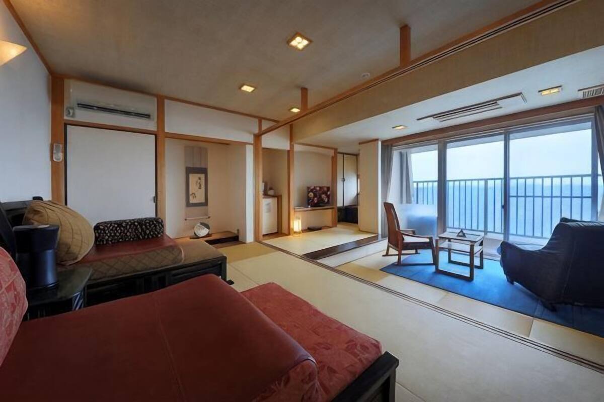 Een kamer met tatami vloerbedekking, een bank, een stoel, een klein tafeltje en een balkon met uitzicht.