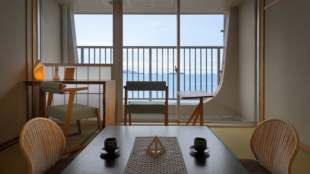 Een kamer met balkon, een tafel met twee stoelen, een lamp en uitzicht op zee.