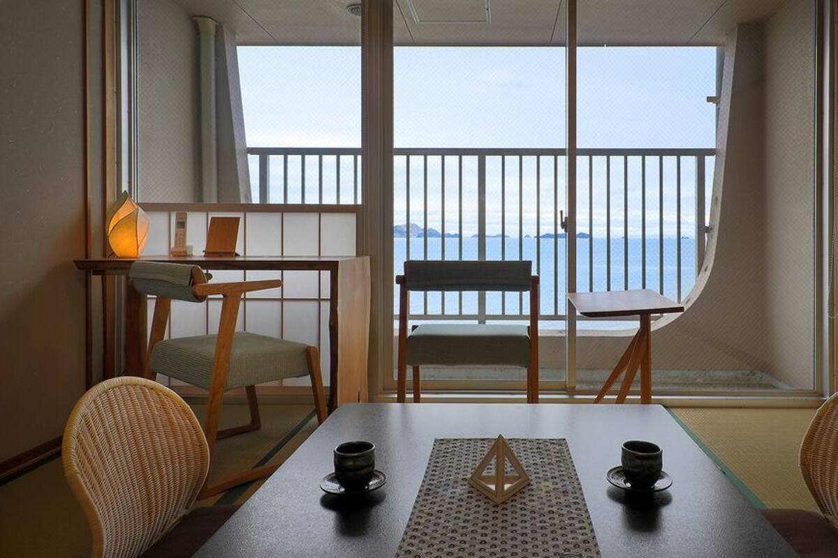 Een kamer met balkon, een tafel met twee stoelen, een lamp en uitzicht op zee.