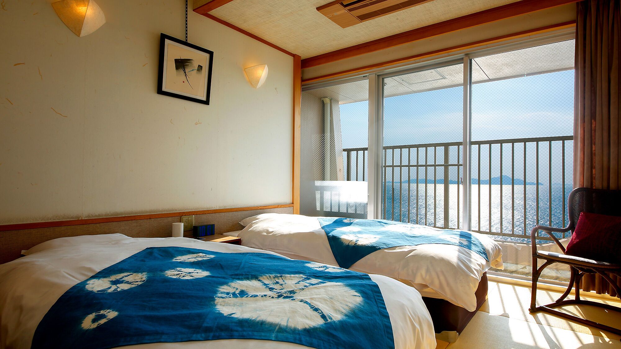 Een hotelkamer met twee bedden, een balkon en uitzicht op zee, plus een stoel.
