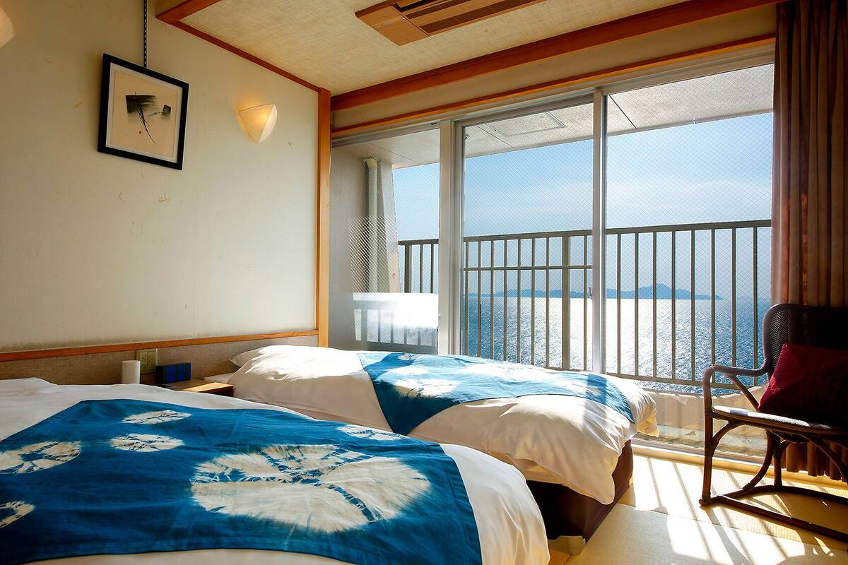 Een hotelkamer met twee bedden, een balkon en uitzicht op zee, plus een stoel.