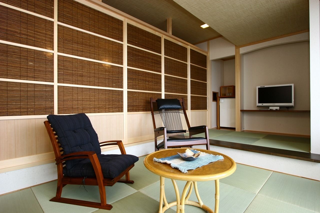 A traditional Japanese room with tatami flooring, a low wooden table, two chairs, and a television on a shelf.