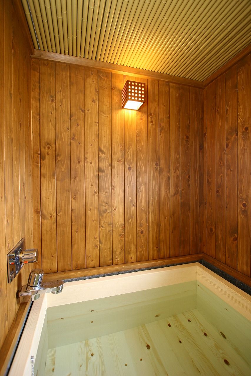 Een houten interieur met een badkuip, een houten plafond en een wandlamp.