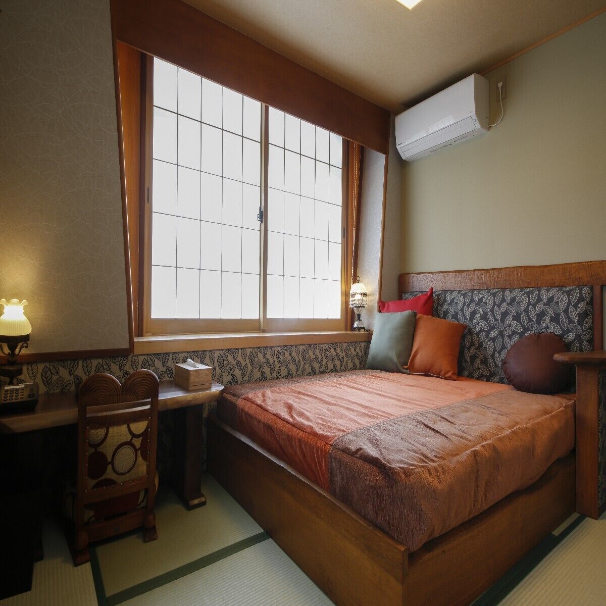 Een kamer met een bed, een bureau, een stoel, een raam en een airconditioning.