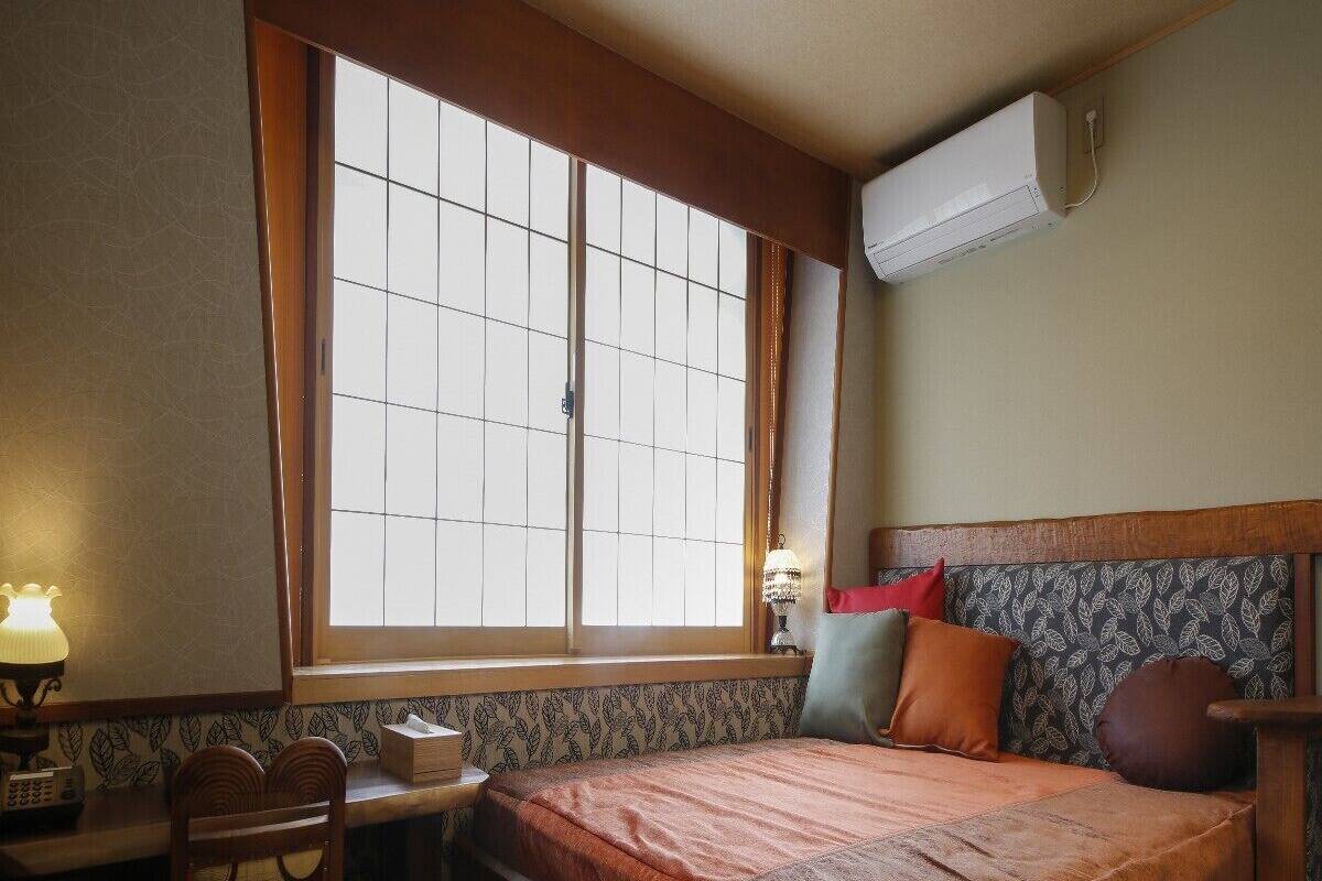 Een kamer met een bed, een bureau, een stoel, een raam en een airconditioning.