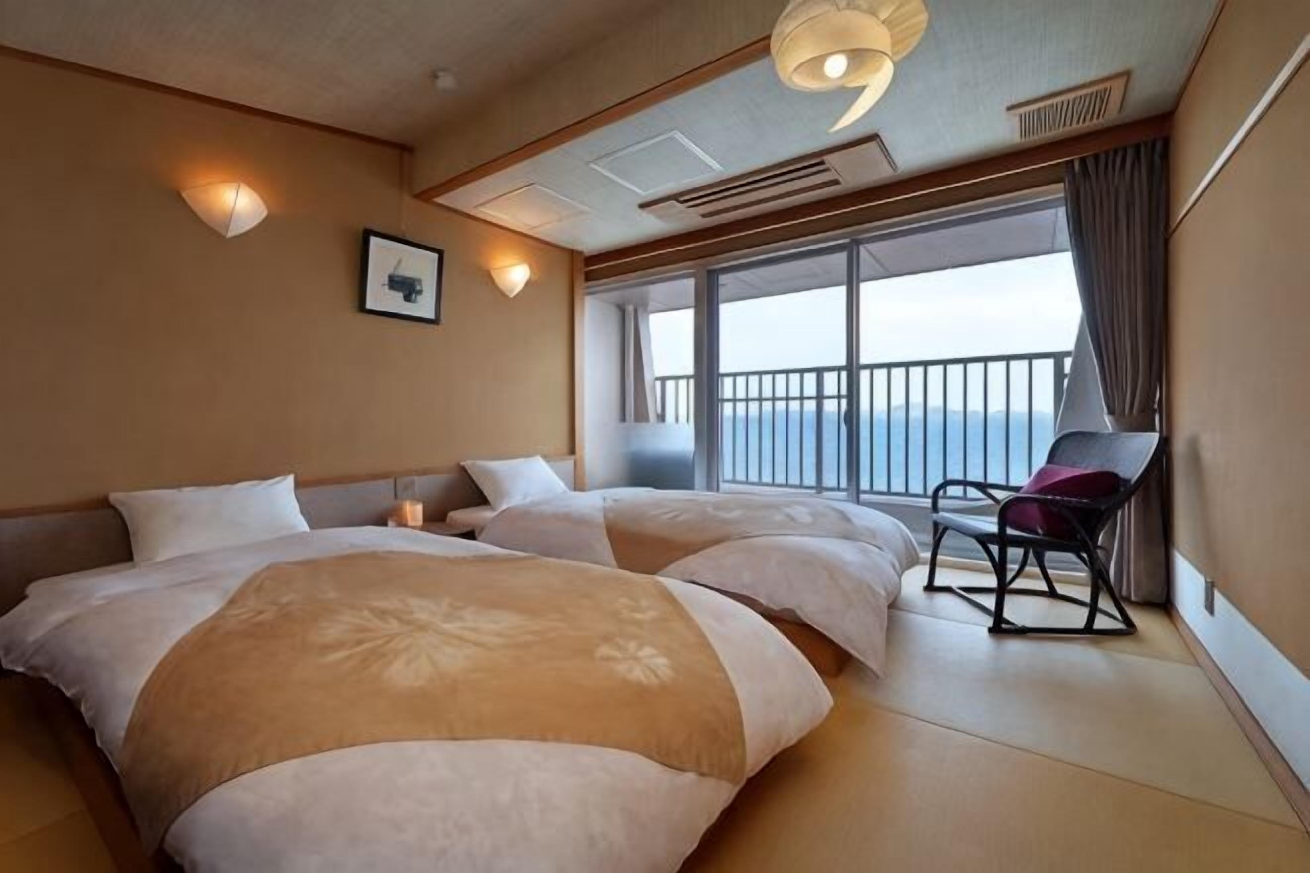 Hotelkamer met twee bedden, een stoel, een groot raam met uitzicht en een plafondlamp.
