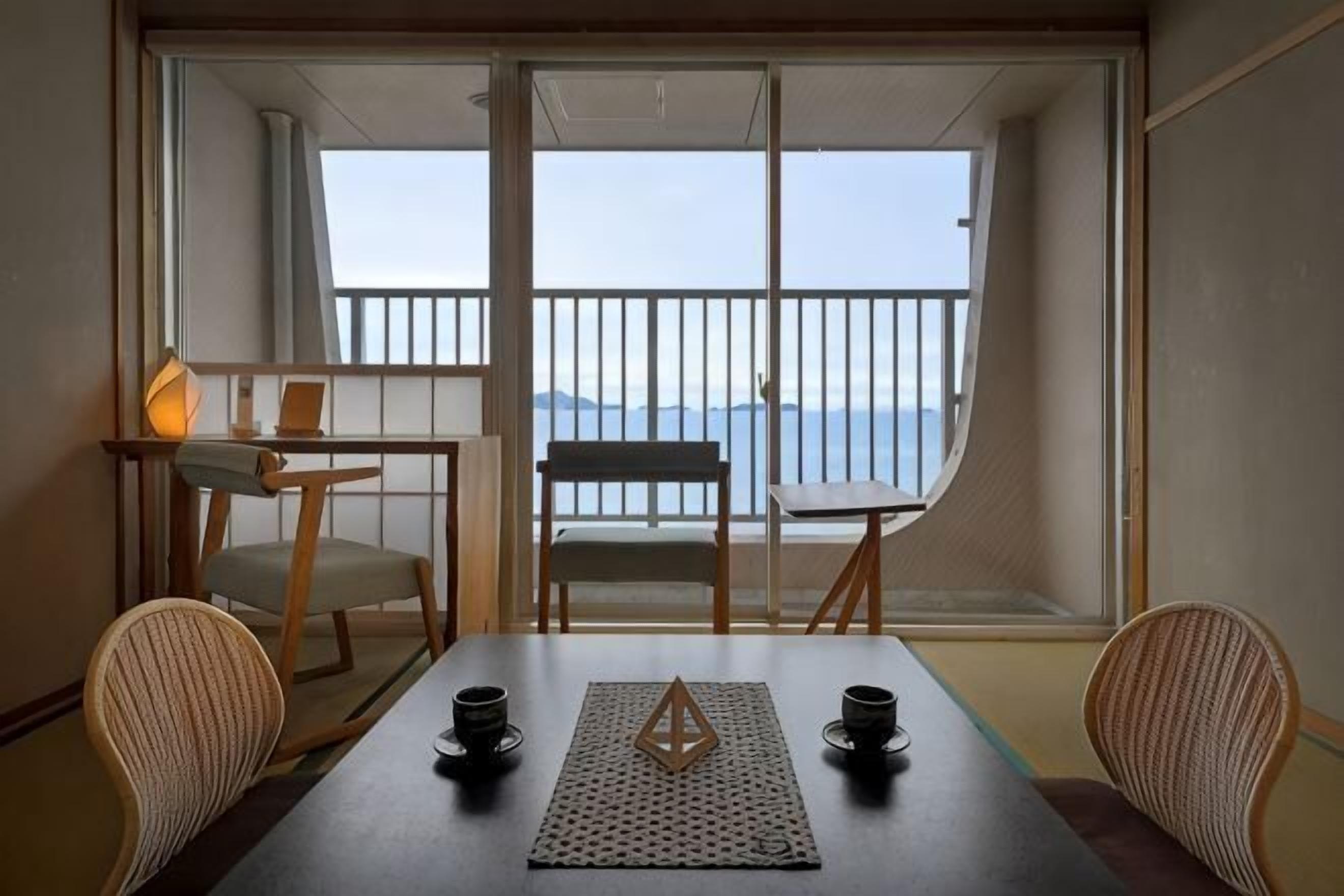 Een balkon met uitzicht op zee, een tafel met stoelen en een kleine tafel met een lamp.