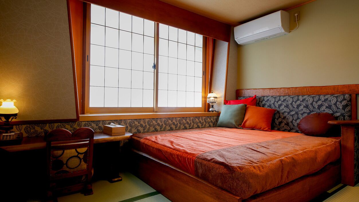 Ein Zimmer mit Bett, Schreibtisch mit Lampe, Stuhl und Fenster mit Blick.