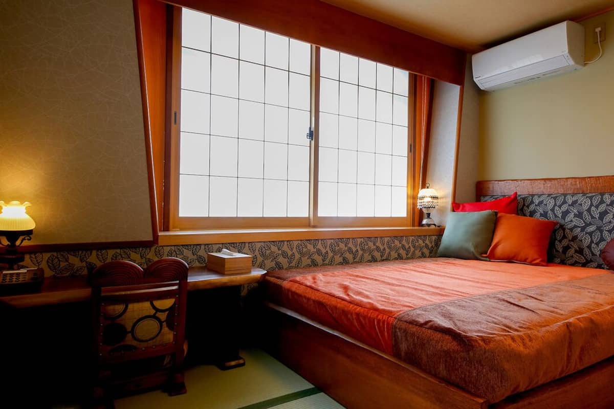 A room with a bed, a desk with a lamp, a chair, and a window with a view.