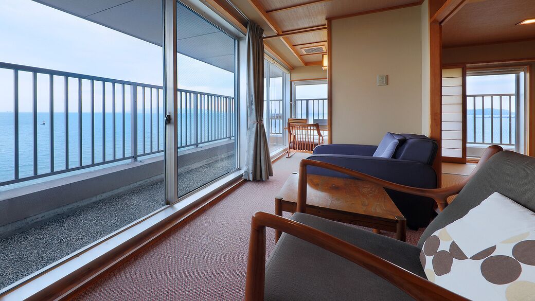 Een balkon met uitzicht op zee, een bed met een blauw hoofdeinde en een houten stoel.
