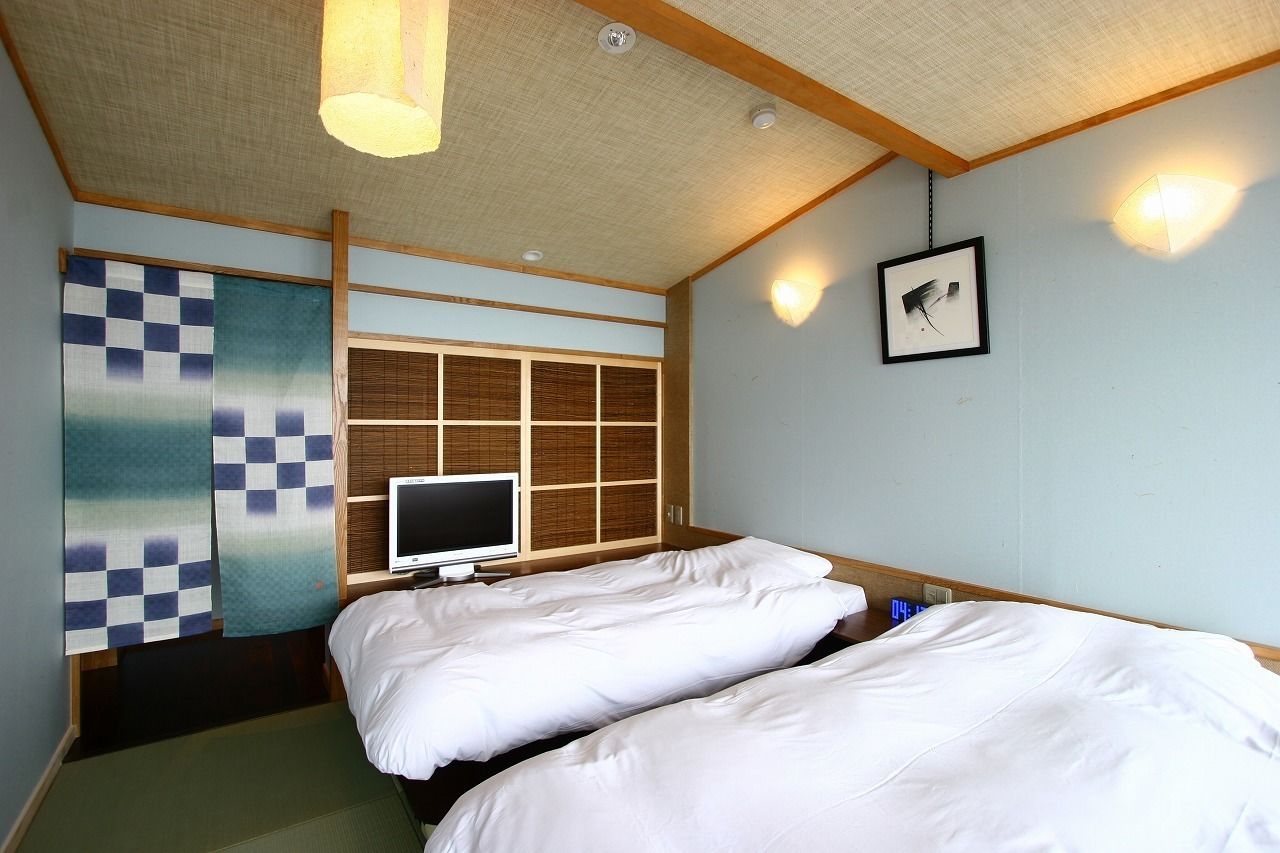 A hotel room with two beds, a television, and traditional Japanese decor.