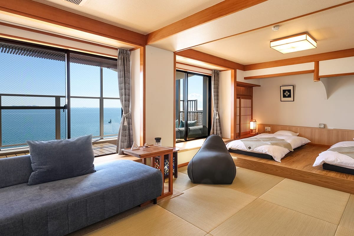 A hotel room with a sofa, two beds, a small table, and a view of the sea.