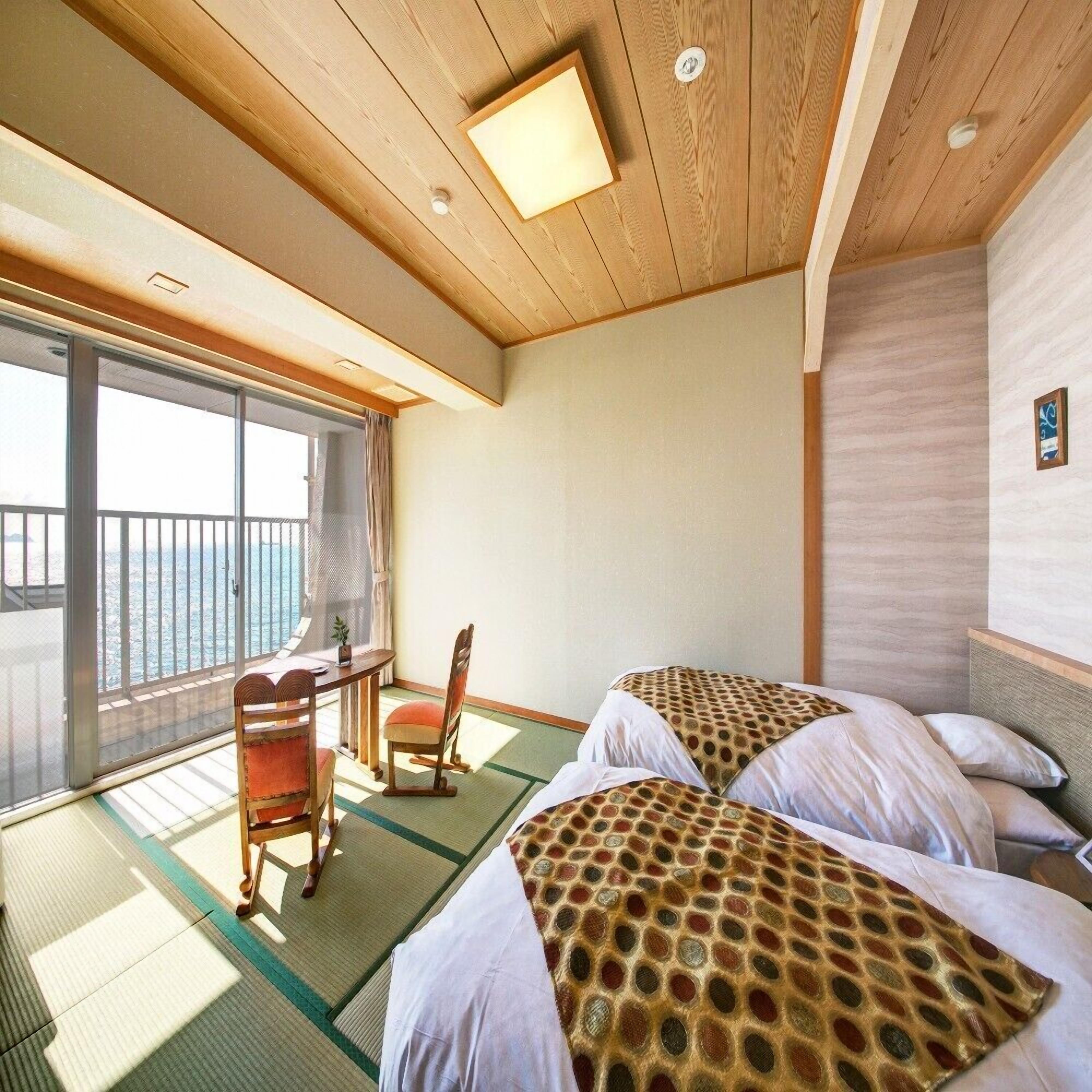 Een kamer met twee bedden, een bureau en een stoel, met uitzicht op zee door grote ramen.