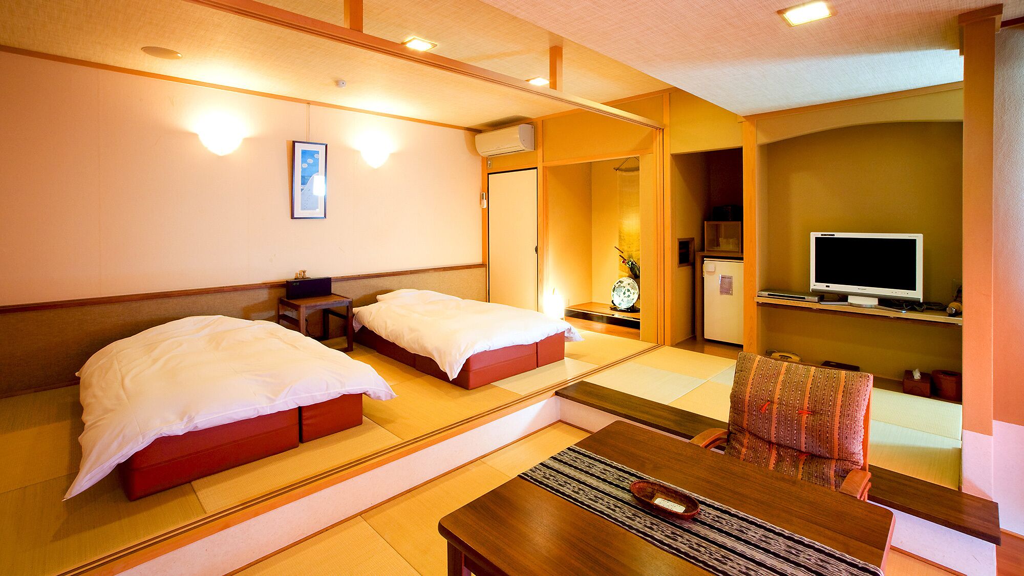 Een hotelkamer met twee bedden, een bureau, een stoel, een televisie en een kitchenette.