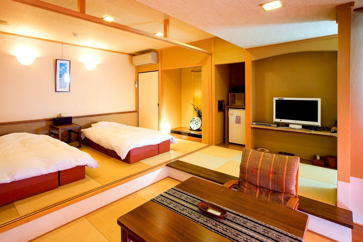 Een hotelkamer met twee bedden, een bureau, een stoel, een televisie en een kitchenette.