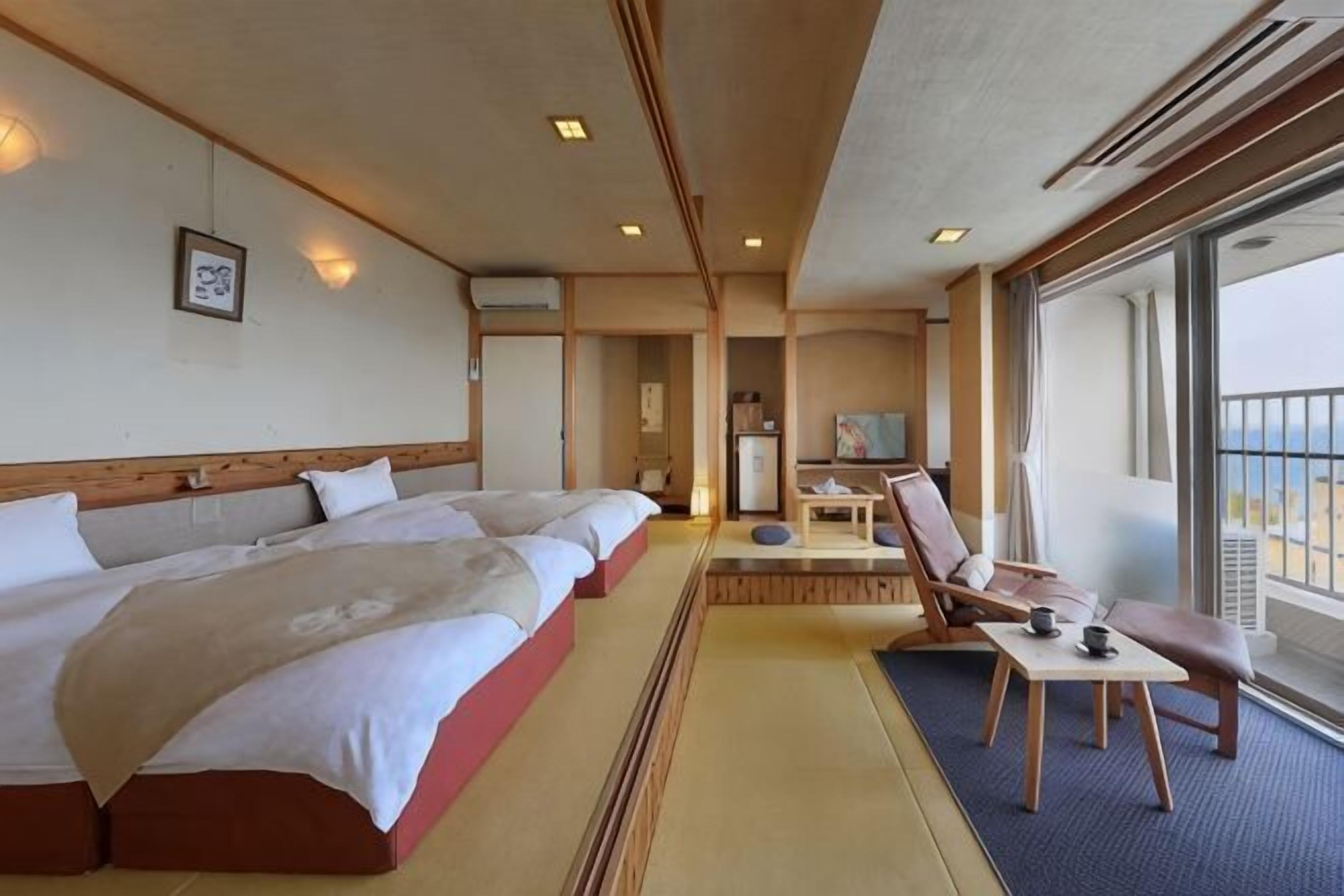 Een hotelkamer met drie bedden, een tafeltje, een stoel en een balkon met uitzicht.