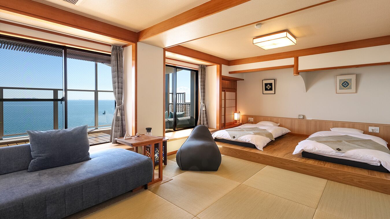 Ein Hotelzimmer mit einer Couch, zwei Betten, einem kleinen Tisch, einem Sessel und Blick aufs Meer.