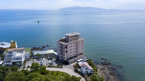 Vista aérea de un hotel costero con varias edificaciones, un estacionamiento y vistas al mar y montañas distantes.