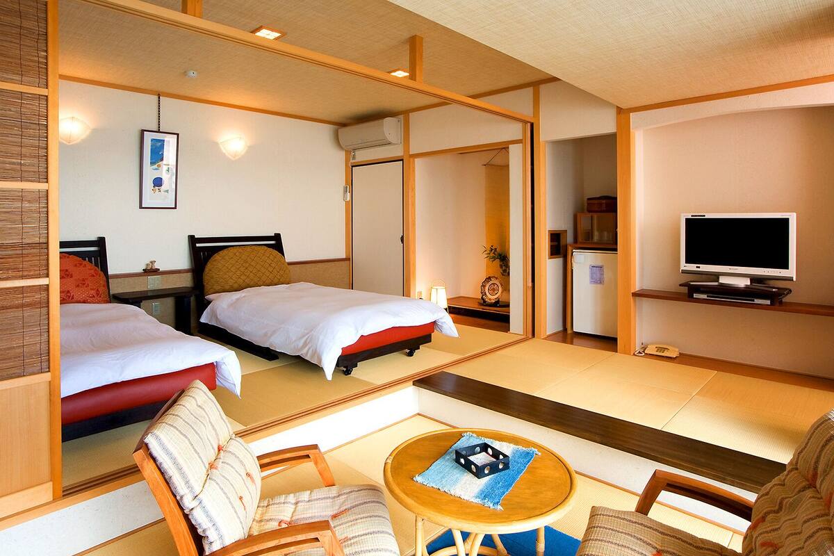 Een hotelkamer met twee bedden, een televisie, een kleine koelkast en een spiegel die de kamer weerspiegelt.