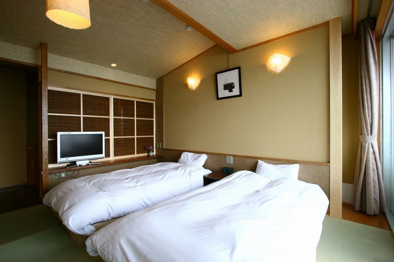 A hotel room with two beds, a television, and a wall-mounted light fixture.
