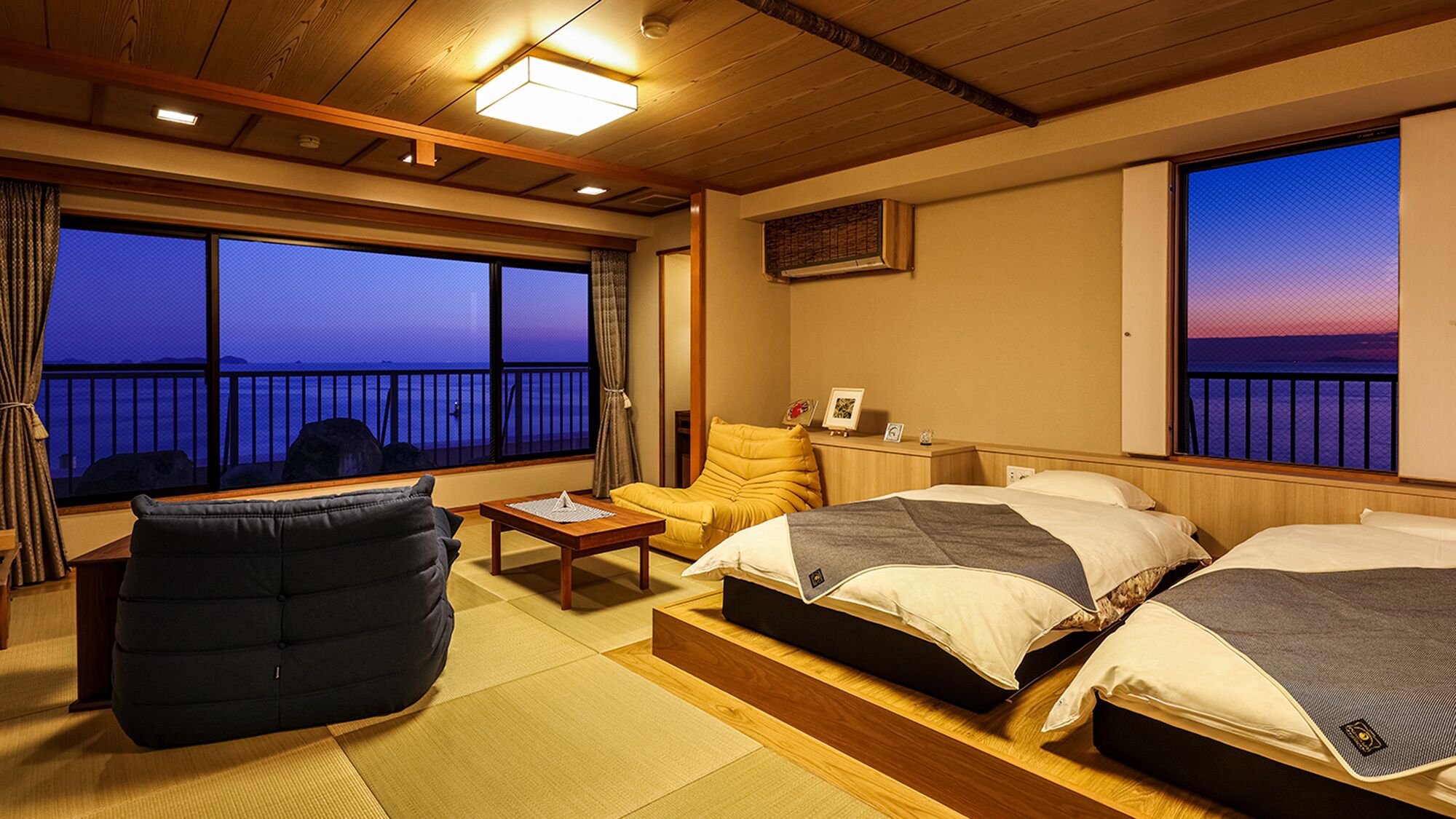 A room with two beds, a chair, a table, and a view of the sea.