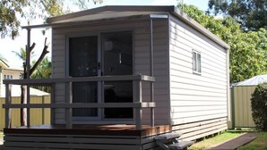A small, single-story mobile home with a front porch and a sliding glass door. - Huntsville Caravan Park (Tinana)