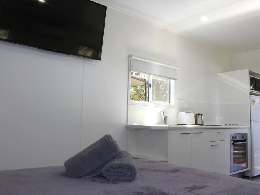 Una habitación moderna y compacta con cama, televisor de pantalla plana en la pared, ventana con vistas, y kitchenette con refrigerador, horno y lavamanos.