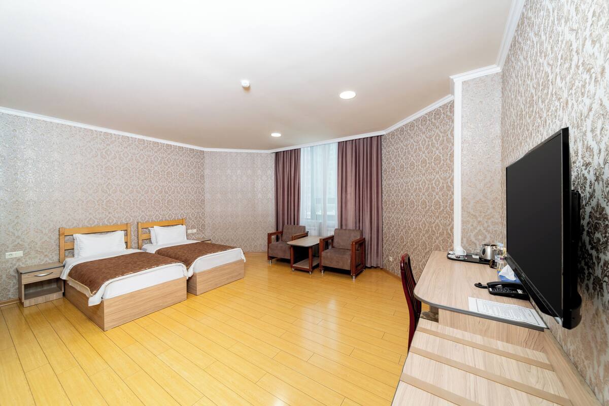 A hotel room with two beds, a desk, a chair, a television, and a window with curtains.