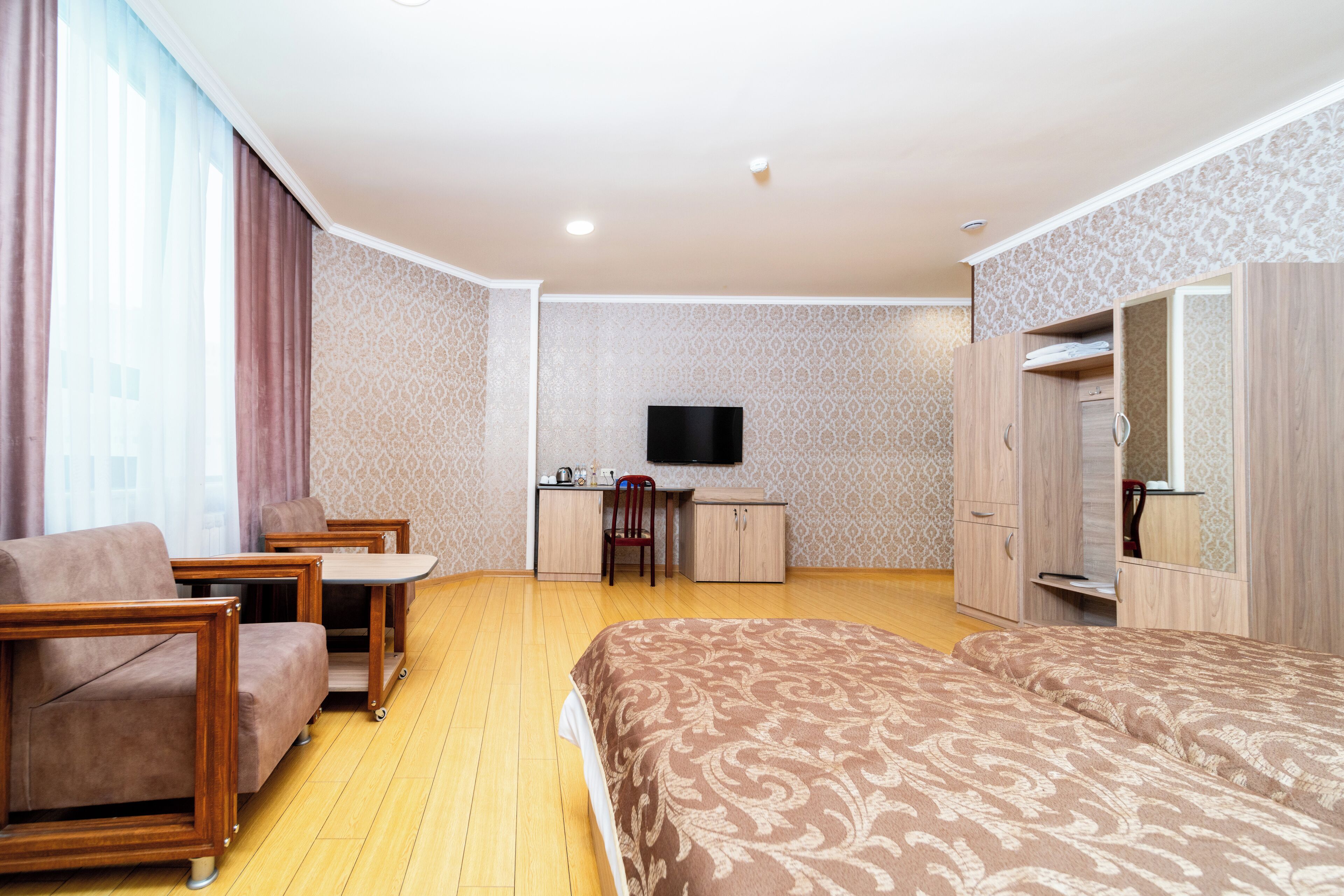 A hotel room with a bed, a desk, a chair, a TV, and a wardrobe.