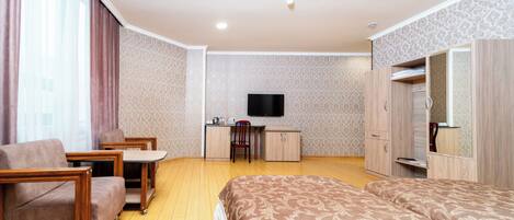 A hotel room with a bed, a desk, a chair, a TV, and a wardrobe.