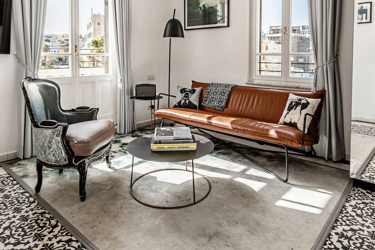 Una sala moderna con un sofá de cuero, un sillón vintage, una mesa de centro y una lámpara de pie.