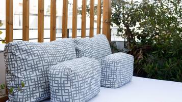 Ein modulares Sofa mit geometrischem Muster, platziert auf einer weißen Fläche, vermutlich einer Terrasse oder einem Balkon, mit einem Holzzaun und Pflanzen im Hintergrund.