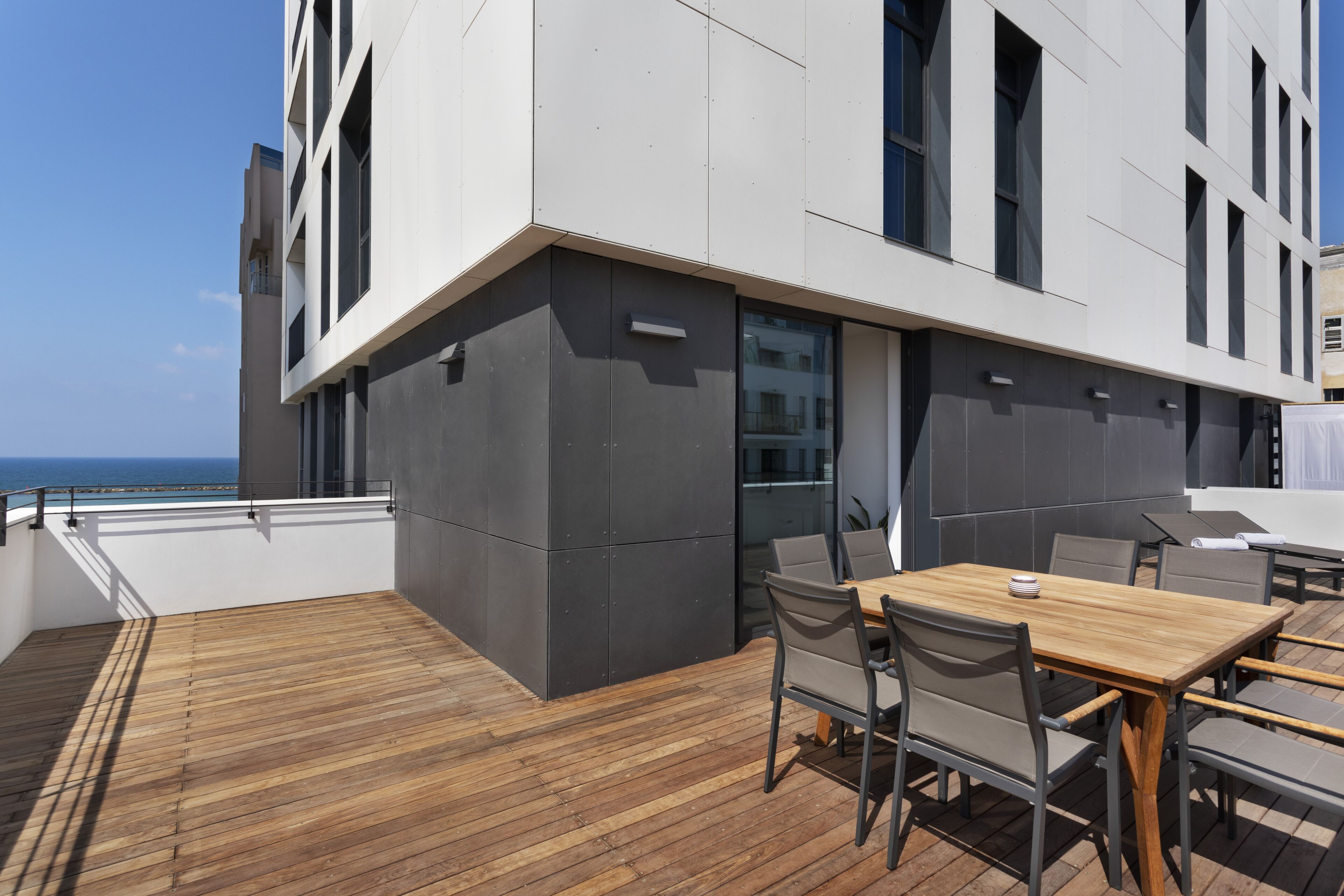 Une terrasse extérieure moderne avec un plancher en bois, une table et des chaises, et une vue sur l’océan.
