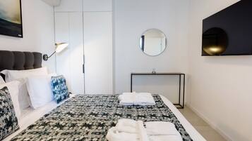 Una habitación de hotel moderna con una cama, una mesita de noche, un espejo y un televisor montado en la pared.