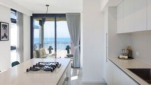 Une cuisine moderne équipée d’une cuisinière à gaz, d’un coin repas avec une table et offrant une vue sur la mer grâce à de grandes fenêtres.