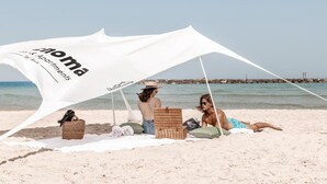 Une scène de plage avec un auvent blanc sur lequel est inscrit le mot « Appartements » et un panier en osier posé sur le sable.
