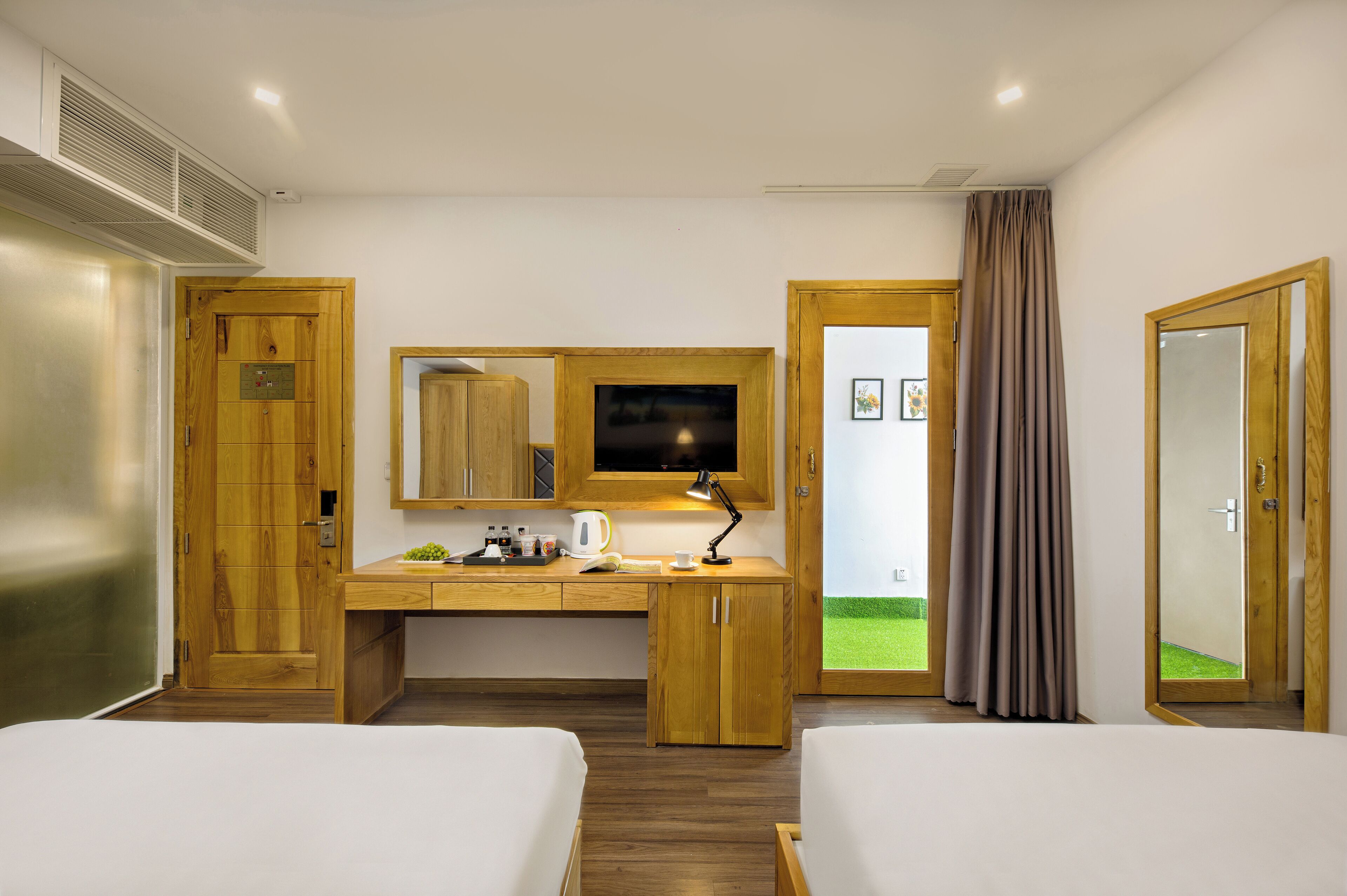 A hotel room with two beds, a desk with a computer, a mirror, and a television.