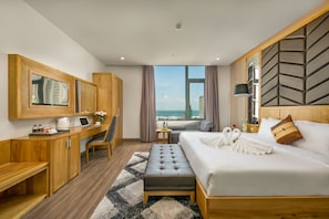 A hotel room with a bed, a desk, a chair, a small table, a sofa, a window with curtains, and a view of the city.