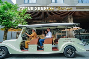 A vintage car with four passengers, parked in front of a boutique hotel named "Grand Sunrise Boutique". - Grand Sunrise Boutique Hotel (Da Nang)