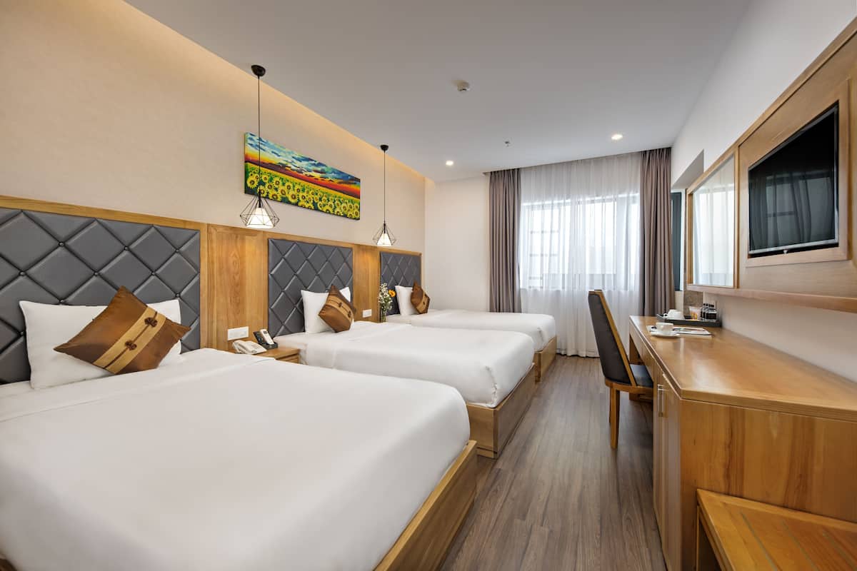 A hotel room with three beds, a desk, a chair, a TV, and a painting on the wall.
