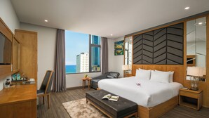 A modern hotel room with a large bed, a desk, a chair, a small table, and a view of the cityscape.