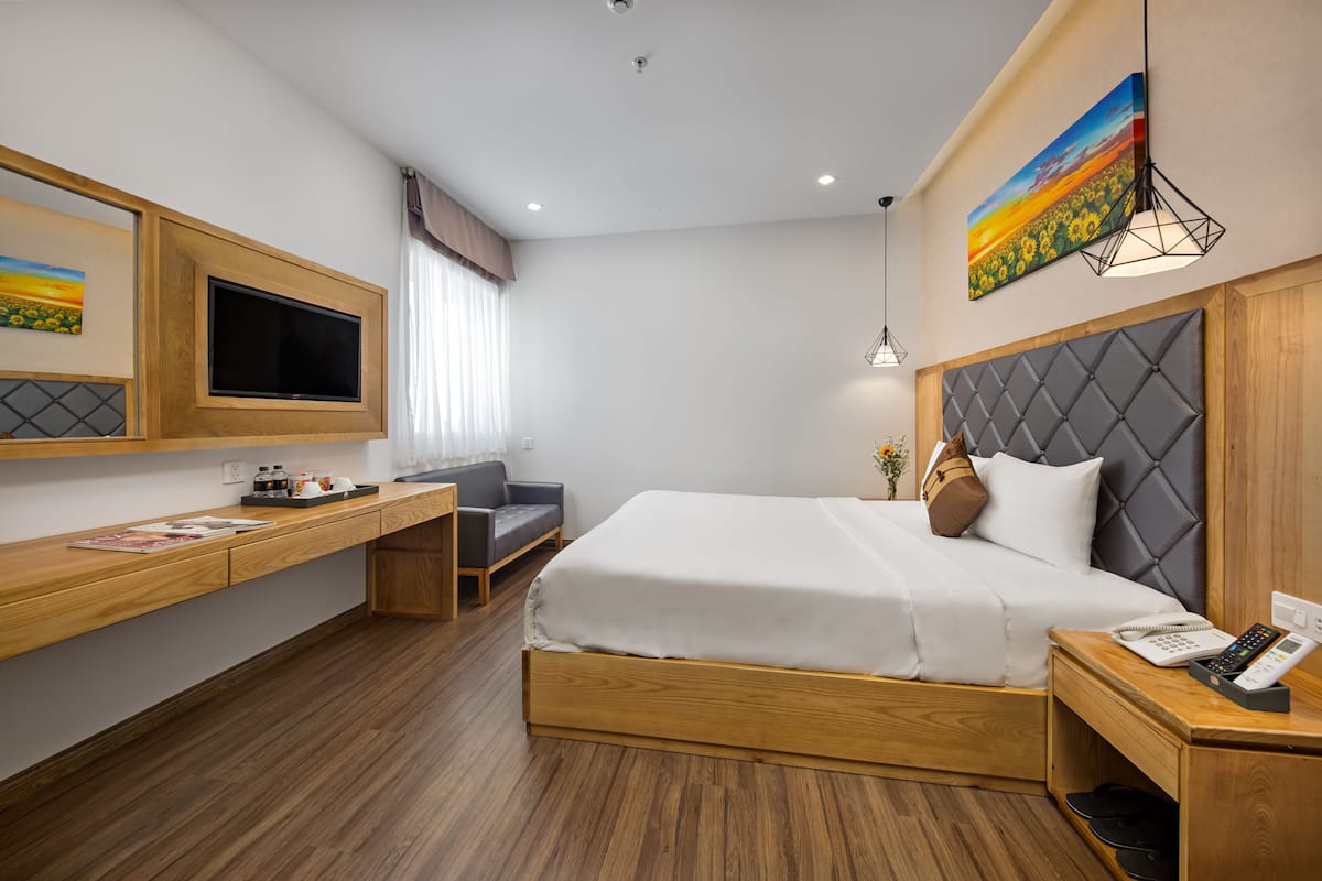 A hotel room with a bed, a desk, a TV, and a painting.