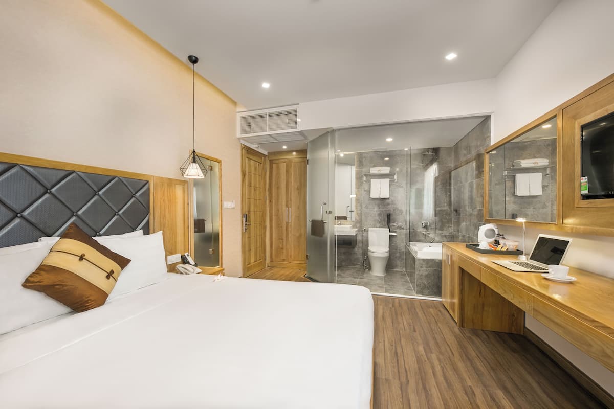A modern hotel room with a bed, a desk, a laptop, and a shower area.
