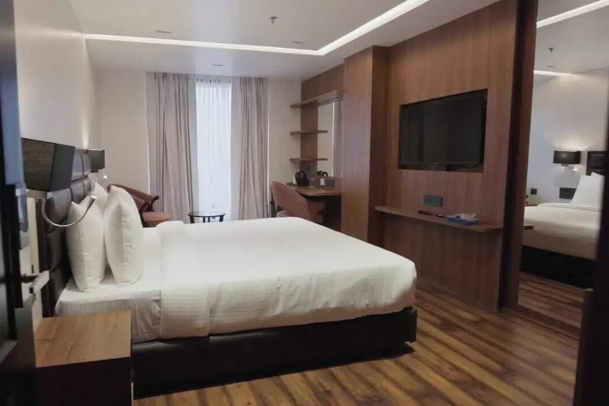 Une chambre d’hôtel avec un grand lit, un bureau, une chaise, une télévision et un miroir.