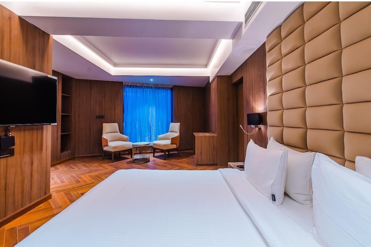 Een moderne hotelkamer met een groot bed, een flatscreen-televisie, houten lambrisering, een gestapeld hoofdeinde en een zithoekje met twee stoelen en een tafeltje.