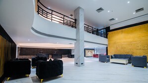 A spacious lobby with a high ceiling, a marble floor, and a central column. There are multiple seating areas with sofas and armchairs. - Hotel Grand Dhillon (Durg)
