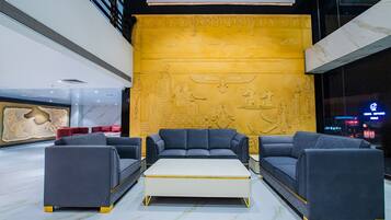 A modern lobby with a large golden wall featuring ancient Egyptian reliefs, a central seating area with sofas and a coffee table, and a marble floor.