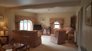 A living room with a sofa, armchairs, a television, and a cabinet with books. - Coldham Cottages (Bedford)