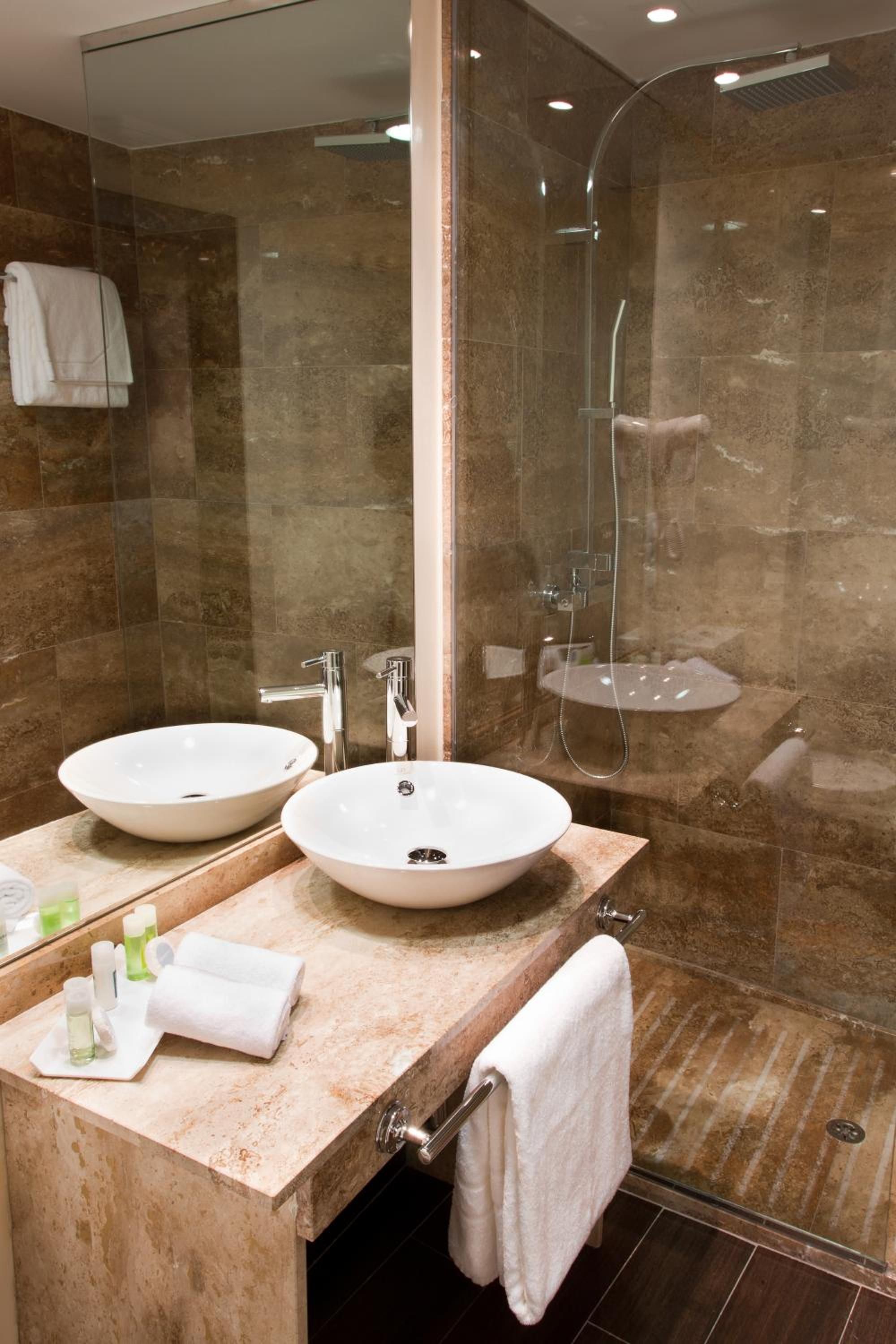 Een badkamer met twee wastafels, een douche en een douchecabine met glazen wanden.